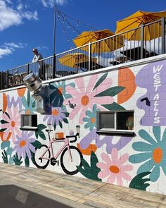 a mural painted on the side of a building with an umbrellas and bike parked outside