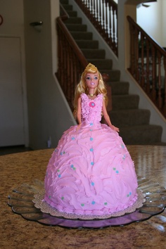 a barbie doll cake sitting on top of a glass plate in front of a stair case