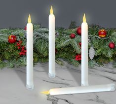 three white candles sitting next to each other on a marble surface with christmas decorations around them