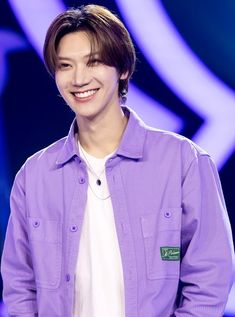 a young man is smiling while wearing a purple shirt and white t - shirt on stage