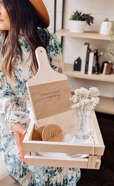 a woman holding a wooden box with personalized items inside and flowers in the bottom