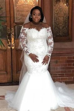 a woman standing in front of a door wearing a wedding dress with long sleeves and an off the shoulder lace top