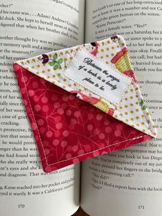 an open book with a piece of fabric on top of it next to a red envelope