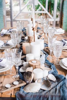 a wooden table topped with lots of white plates and glasses next to a tall candle