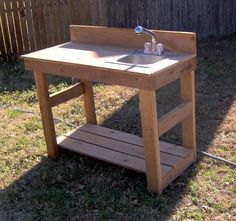 a wooden table with a sink on it in the grass next to a fenced area