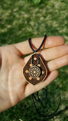 a hand holding a small wooden pendant with an intricate design on it's side