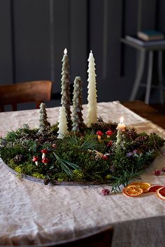 a table topped with candles surrounded by evergreen and pine cones