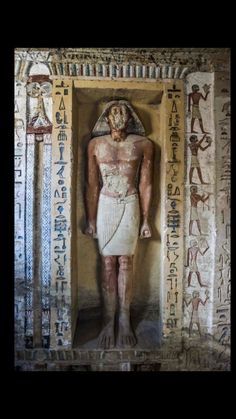 an ancient egyptian statue in the corner of a room with paintings and writing on it