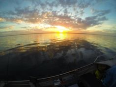 the sun is setting over the water from a boat