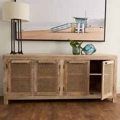 a wooden sideboard sitting on top of a hard wood floor next to a lamp