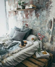 a bed with pillows and blankets on top of it in front of a wall that has peeling paint