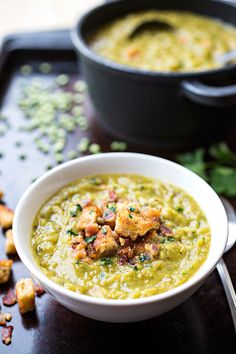 there is a bowl of soup on the table next to some bread croutons