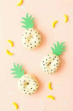 three donuts decorated to look like pineapples and bananas on a pink background