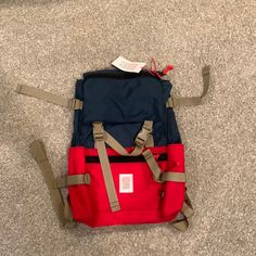 a red and blue backpack sitting on the floor next to a pair of brown straps