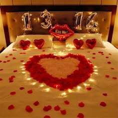 a bed decorated with red rose petals and balloons in the shape of a heart for valentine's day