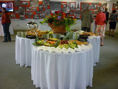 a table covered with lots of food and people looking at pictures on the wall behind it