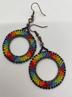 two pairs of multicolored beaded hoop earrings on white surface with gold hooks