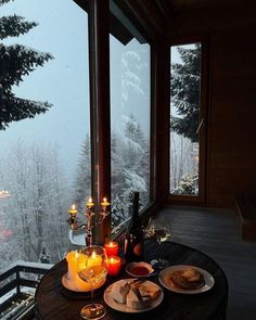 a table with food and candles on it in front of a window overlooking the snow covered mountains