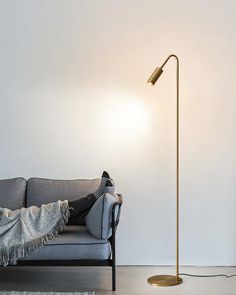 a person laying on a couch under a lamp next to a gray sofa with a blanket draped over it