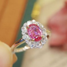 a close up of a person holding a ring with a pink and white diamond in it