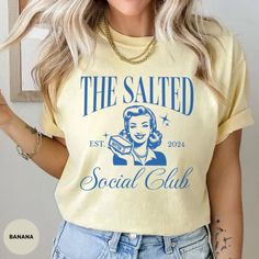 Embrace vintage charm with our "The Salted Social Club" Comfort Colors T-Shirt and Sweatshirt. Featuring a retro-inspired design with a classic nod to the year 2024, this stylish graphic showcases a woman holding butter, making it perfect for those who love a touch of nostalgia. Available in the soft and durable Comfort Colors fabric, this shirt offers long-lasting comfort and a unique, worn-in look. Ideal for casual outings, social gatherings, or just lounging at home, add a vintage flair to yo Vintage Yellow T-shirt With Funny Print, Nostalgic Cotton Tops With Letter Print, Vintage Yellow Crew Neck Shirt, Vintage Crew Neck Shirt With Letter Print, Vintage Relaxed Fit Top With Letter Print, Vintage Tops With Letter Print And Relaxed Fit, Vintage Cotton Shirt With Letter Print, Yellow Retro Shirt With Letter Print, Spring Vintage Shirt With Letter Print