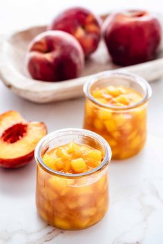 two jars filled with peaches sitting on top of a table next to sliced peaches