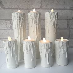 five white candles sitting next to each other in front of a brick wall with icing on them