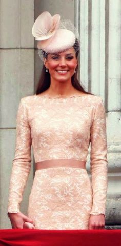 a woman in a pink dress and hat standing next to a red ribbon on the steps