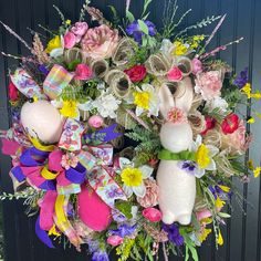 an easter wreath with flowers and bunnies hanging from the front door, decorated with ribbons