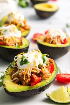 avocados stuffed with meat, cheese and vegetables on a white surface next to limes