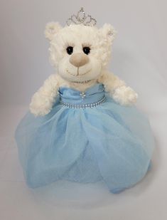 a white teddy bear dressed up in a blue dress with a tiara on it's head