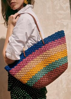 a woman carrying a multicolored crocheted bag in front of a wall