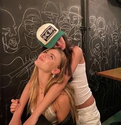 two young women hugging each other in front of a chalkboard wall with drawings on it