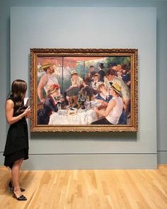 a woman standing in front of a painting with people eating and drinking at a table