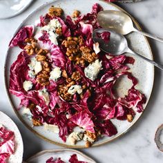 a white plate topped with red cabbage and walnuts next to two plates of food