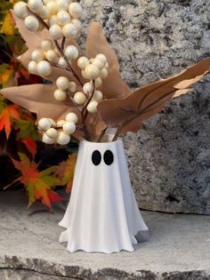 a white vase filled with berries and leaves on top of a stone slab next to a rock wall