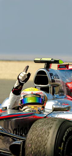 a man driving a silver race car on top of a dirt track with his hand in the air