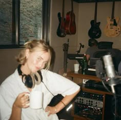 a woman holding a coffee cup in front of a recording studio with guitars on the wall