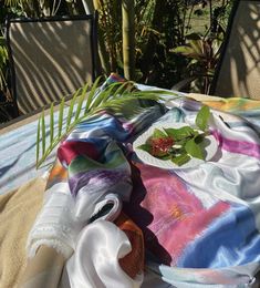 a table topped with a white plate covered in green leaves and cloths next to a palm tree