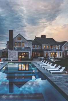 a large house with a swimming pool and lounge chairs around the perimeter, at dusk