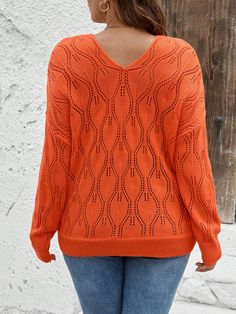 a woman wearing an orange sweater and jeans is standing in front of a white wall