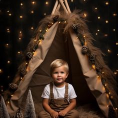 a little boy that is sitting in front of a teepee