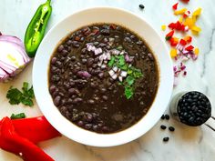 a white bowl filled with black beans next to red peppers, onions and jalapenos