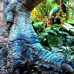 an animal that is standing in the dirt near some trees and plants with leaves on it's trunk