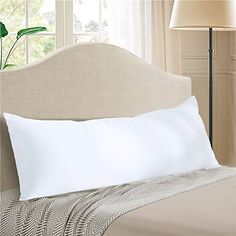 a white pillow on top of a bed next to a beige headboard and lamp