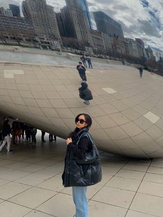 a woman standing in front of a large mirror ball with buildings in the background and people walking around