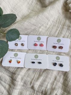 four pairs of earrings sitting on top of a white card next to a green plant