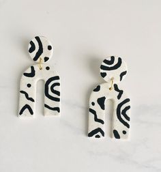 two white and black ceramic earrings with designs on them sitting on a marble countertop