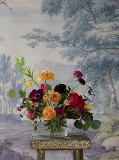 a vase filled with lots of colorful flowers on top of a wooden table next to a wall