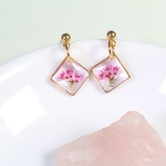 These dainty, handmade resin pressed flower earrings feature real pink heather flowers in a gold or silver diamond-oriented square setting. Real flowers are carefully preserved, clipped, then cured in several layers of resin. Small and lightweight, classy enough for a wildflower wedding, but tasteful enough that they're perfect for everyday wear.  Dimensions: From stud to bottom of earring - 1 inch Width - just over a 1/2 inch Ball studs are hypoallergenic and each pair comes with a steel and si Dainty Pink Gold Flower Jewelry, Dainty Rose Gold Birth Flower Earrings, Rose Gold Flower Earrings With Pressed Flowers For Gift, Rose Gold Pressed Flower Earrings Gift, Dainty Handmade Rectangular Jewelry, Handmade Dainty Rectangular Jewelry, Dainty Hypoallergenic Rectangular Jewelry, Botanical Jewelry With Pressed Flowers, Botanical Drop Earrings With Birth Flower